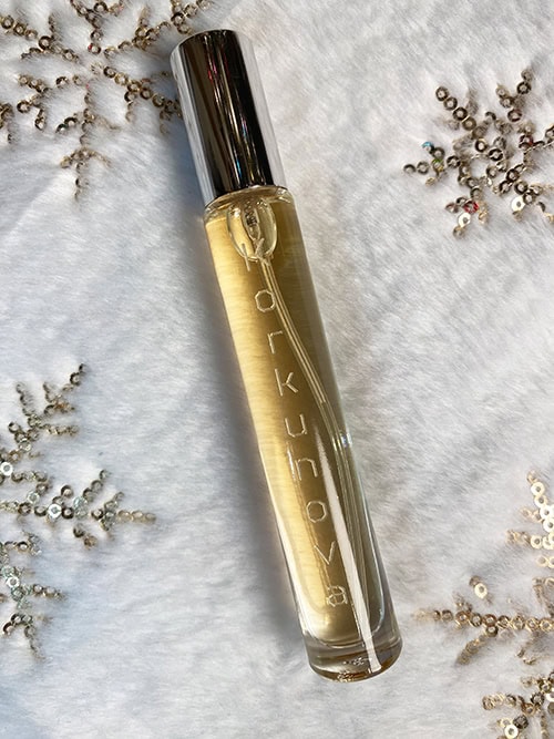 A bottle of Korkunova Vanilla Dream pheromone perfume laying on a plush white fabric with gold snowflakes