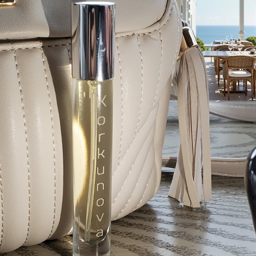 A bottle of Korkunova Vanilla Dream perfume next to a purse sitting on a table in an open-air cafe along the coast of Portugal